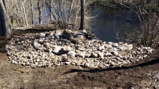 Stenar som ligger i cirkelformation vid stranden till ett vattendrag.