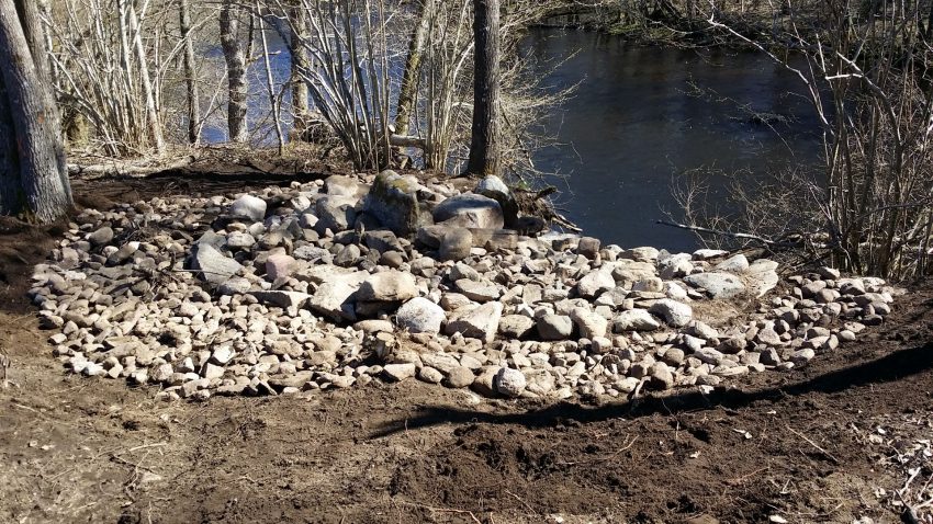 Stenar som ligger i cirkelformation vid stranden till ett vattendrag.
