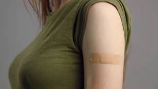 Kvinna med grön tröja och plåster på överarmen.