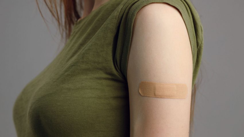 Kvinna med grön tröja och plåster på överarmen.