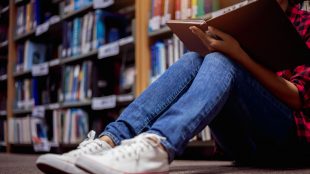 Student sitter på golvet och läser i ett bibliotek.