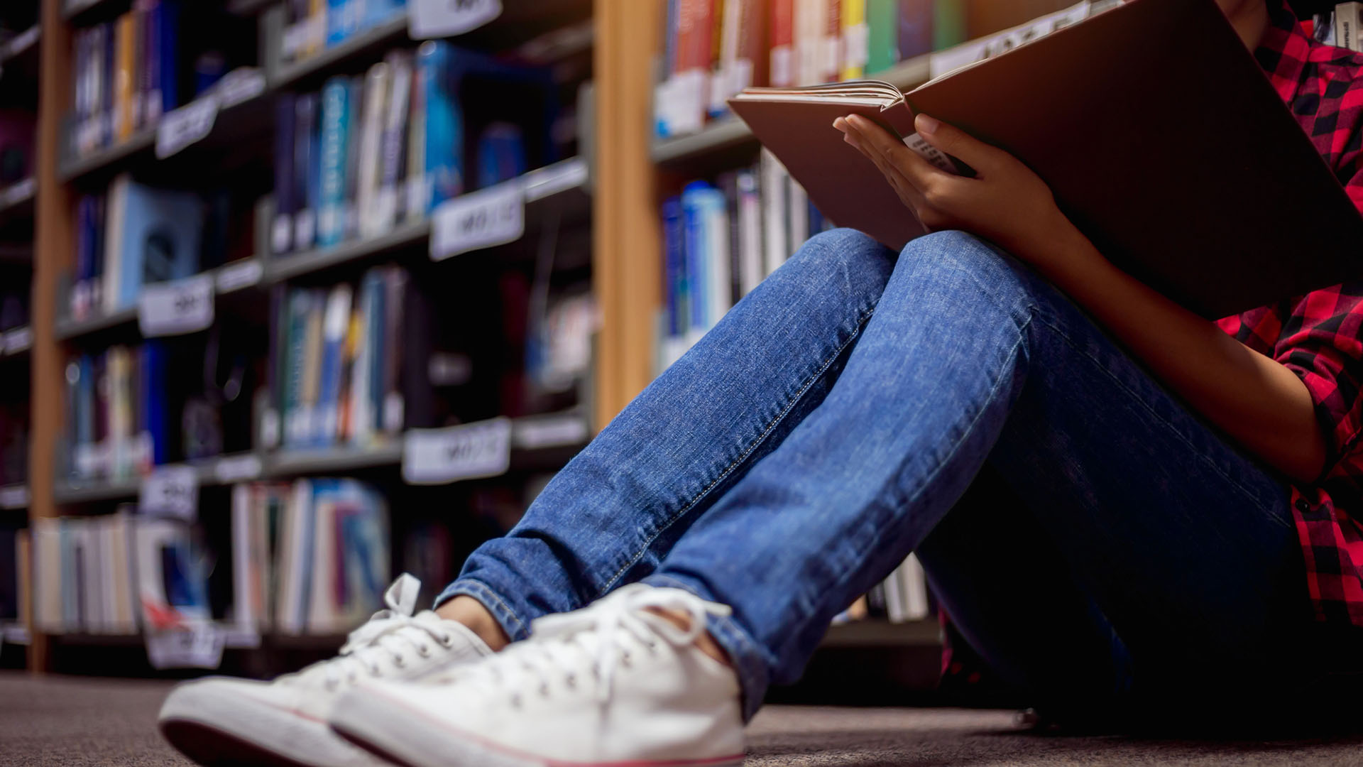 Student sitter på golvet och läser i ett bibliotek.
