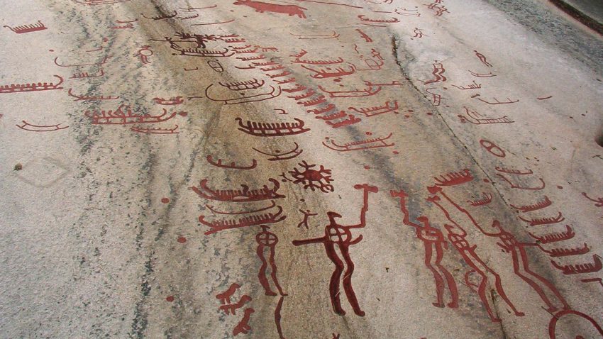 Ristningar med manliga figurer, båtar och djur på en stenhäll.