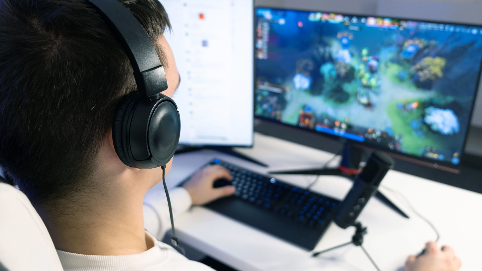 Tonårskille med hörlurar sitter framför datorskärm och spelar.