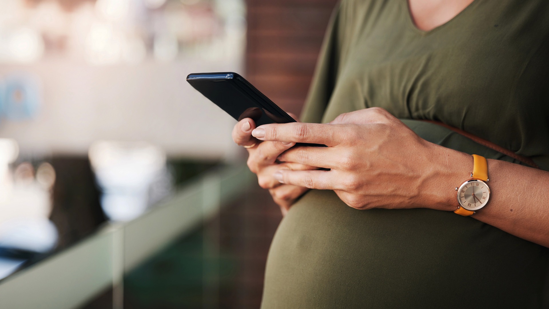 Gravid kvinna står ute på en balkong med mobil i handen.
