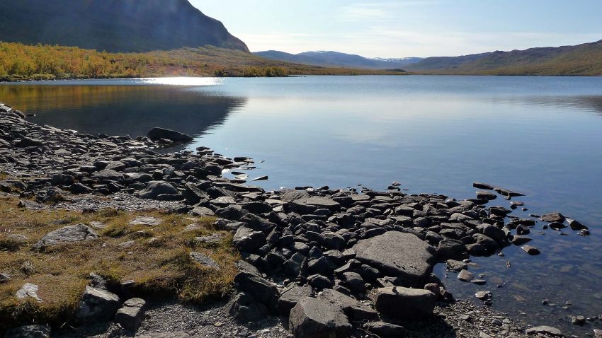 Fjällsjö med spegelblankt vatten och berg i bakgrunden.
