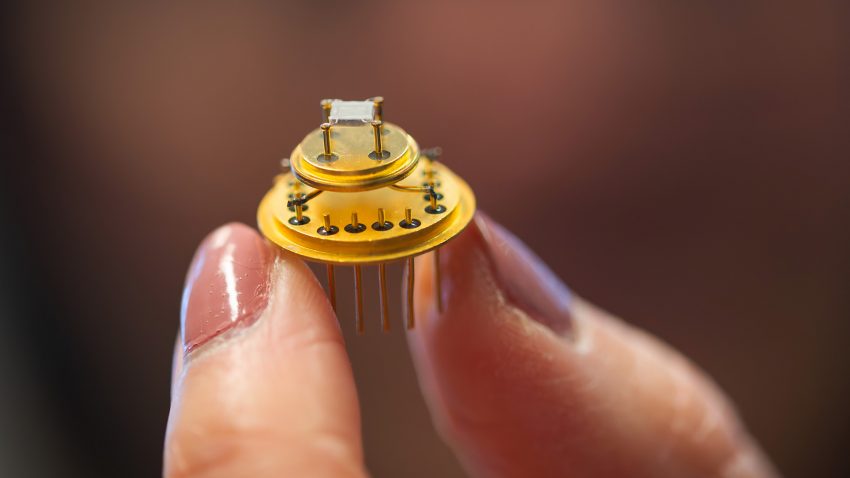 Forskare håller upp en rund guldfärgad sensor.