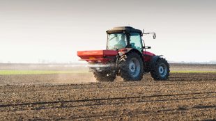 Traktor sprider konstgjort gödsel på åker.