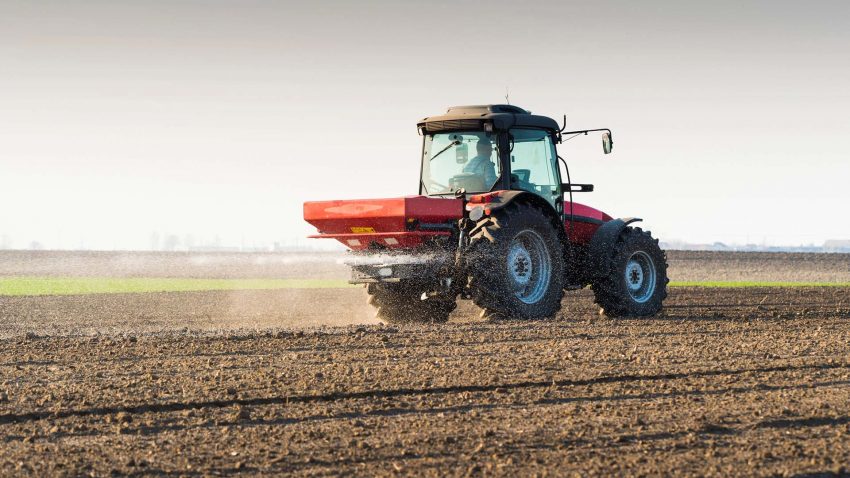 Traktor sprider konstgjort gödsel på åker.
