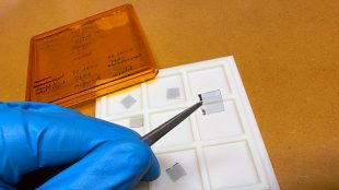 Pincett håller i en tunn genomskinlig fyrkant med metallkant.