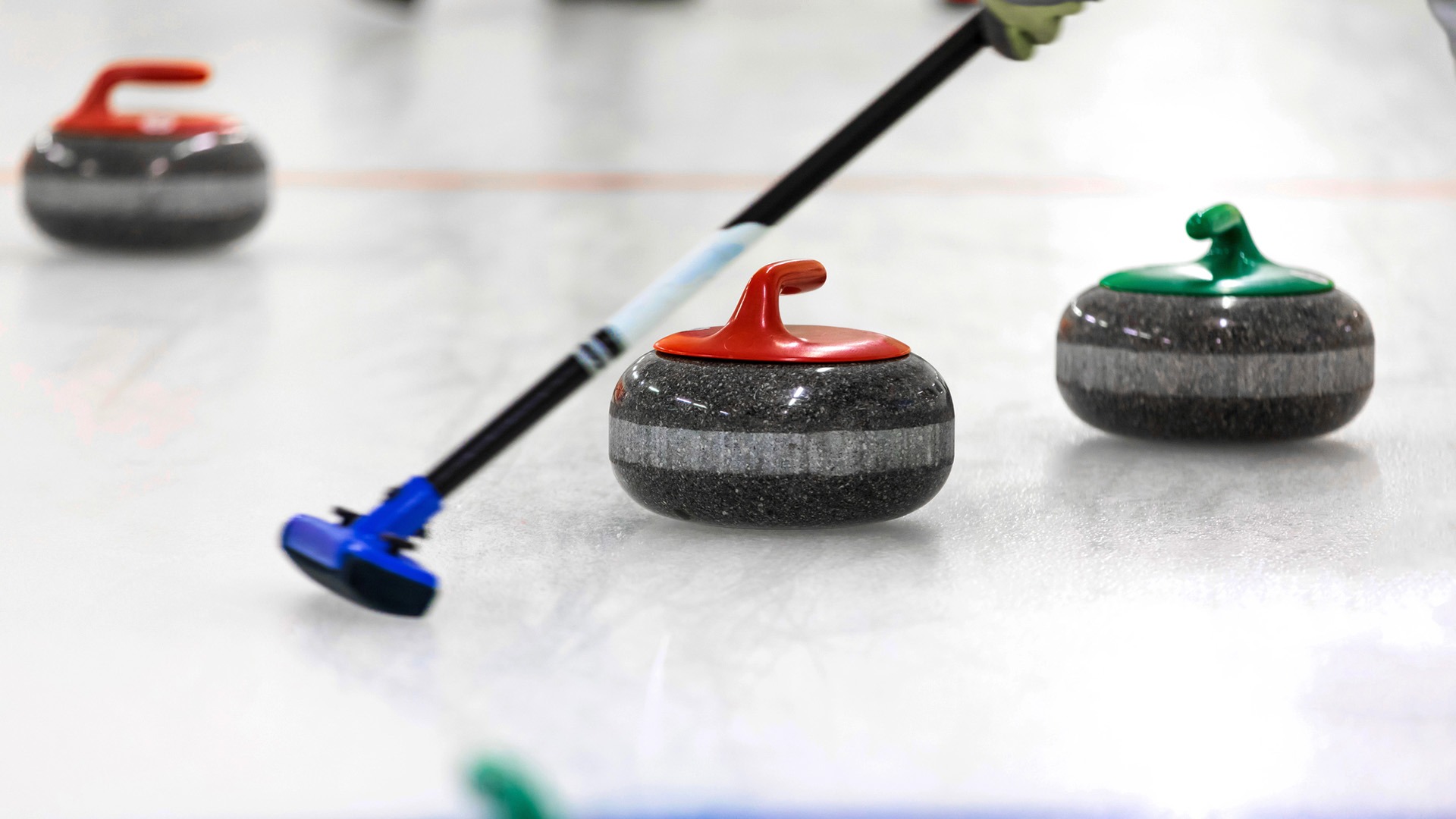 Tre curlingklot och en borste på is