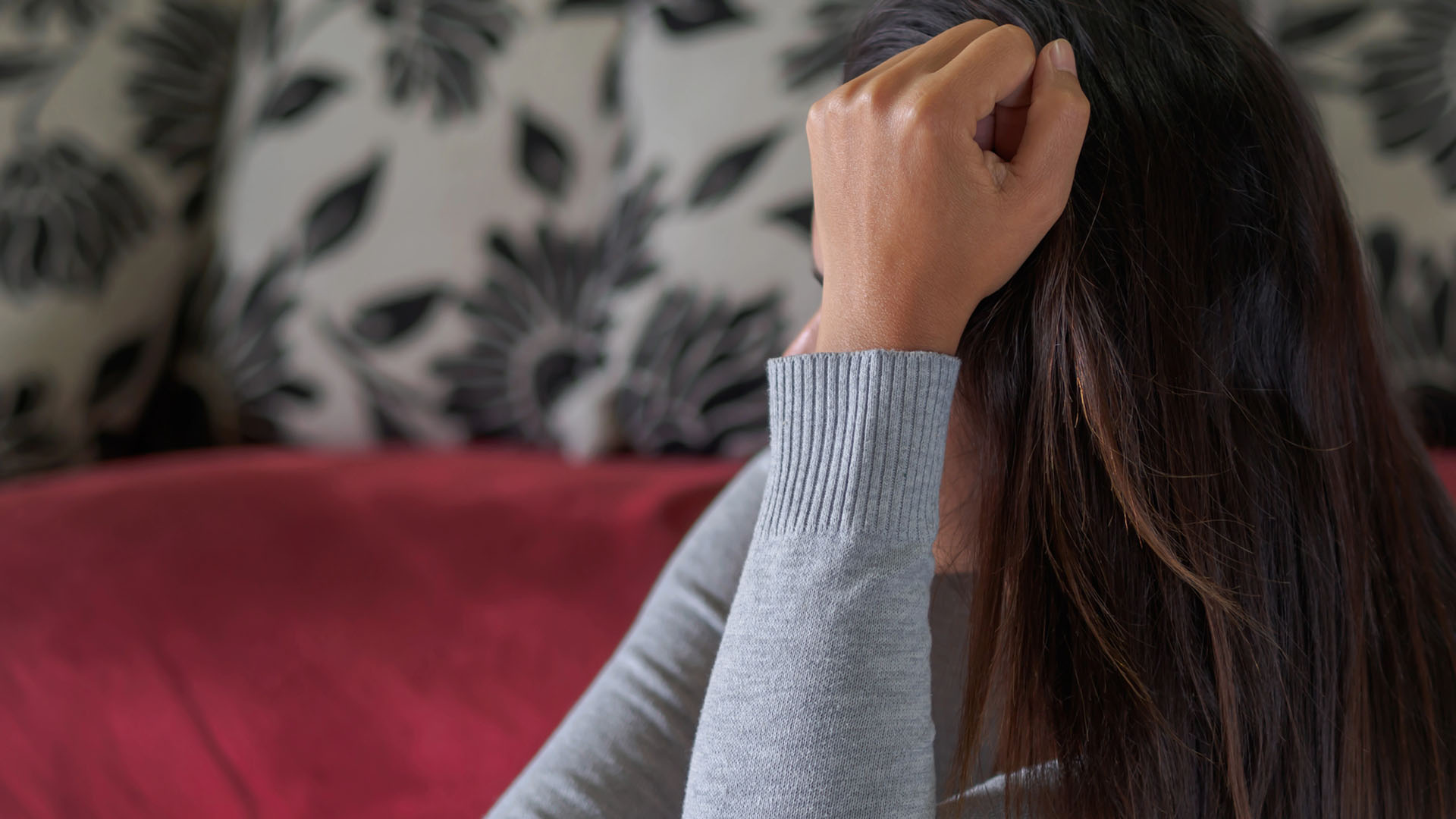 Kvinna i en röd soffa med hand mot huvudet.