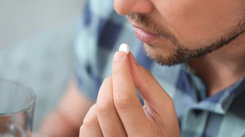 Man håller i ett vattenglas och ett ett piller.