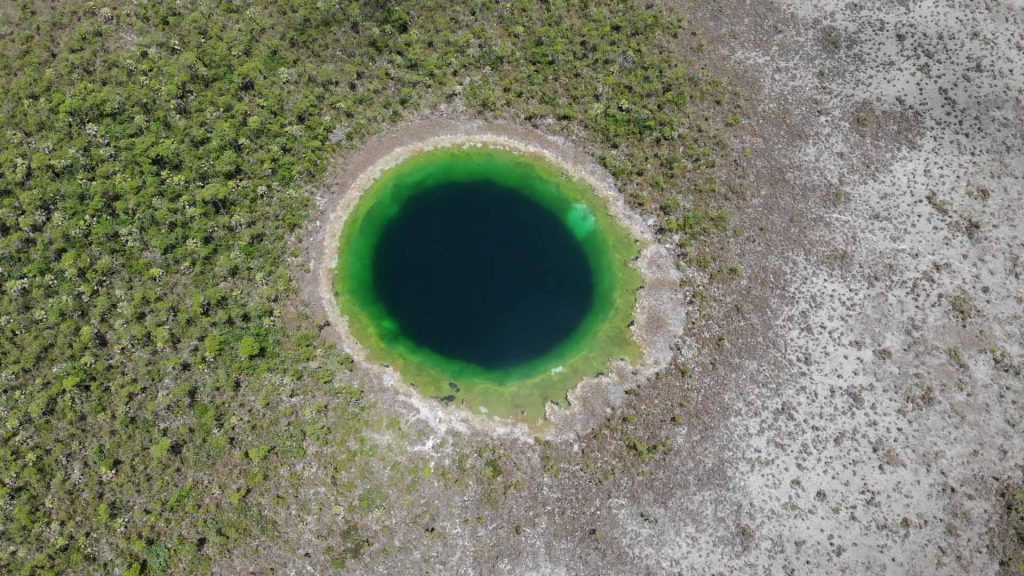 Bild tagen uppifrån, grottan ses som ett runt grönblått hål.