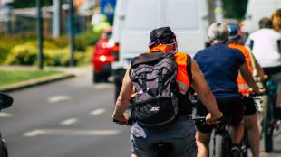 Människor cyklar på rad i stadsmiljö, sommartid.