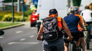 Människor cyklar på rad i stadsmiljö, sommartid.