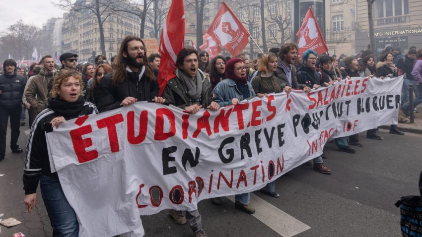 Unga människors marscherar och bär en banderoll med röda och svarta bokstäver.