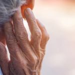 En gammal person sedd bakifrån, håller upp rynkig hand vid öra.