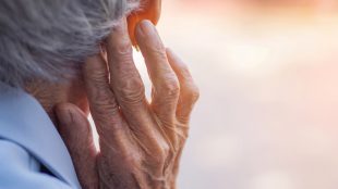 En gammal person sedd bakifrån, håller upp rynkig hand vid öra.