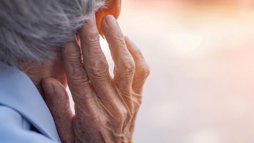 En gammal person sedd bakifrån, håller upp rynkig hand vid öra.
