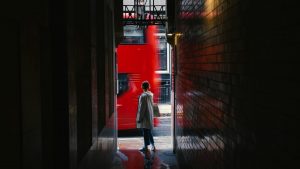 Kvinna i gränd, röd dubbeldäckare far förbi bakom henne.