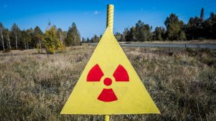 Gul skylt med röd symbol för radioaktivitet. Gräs i bakgrunden.