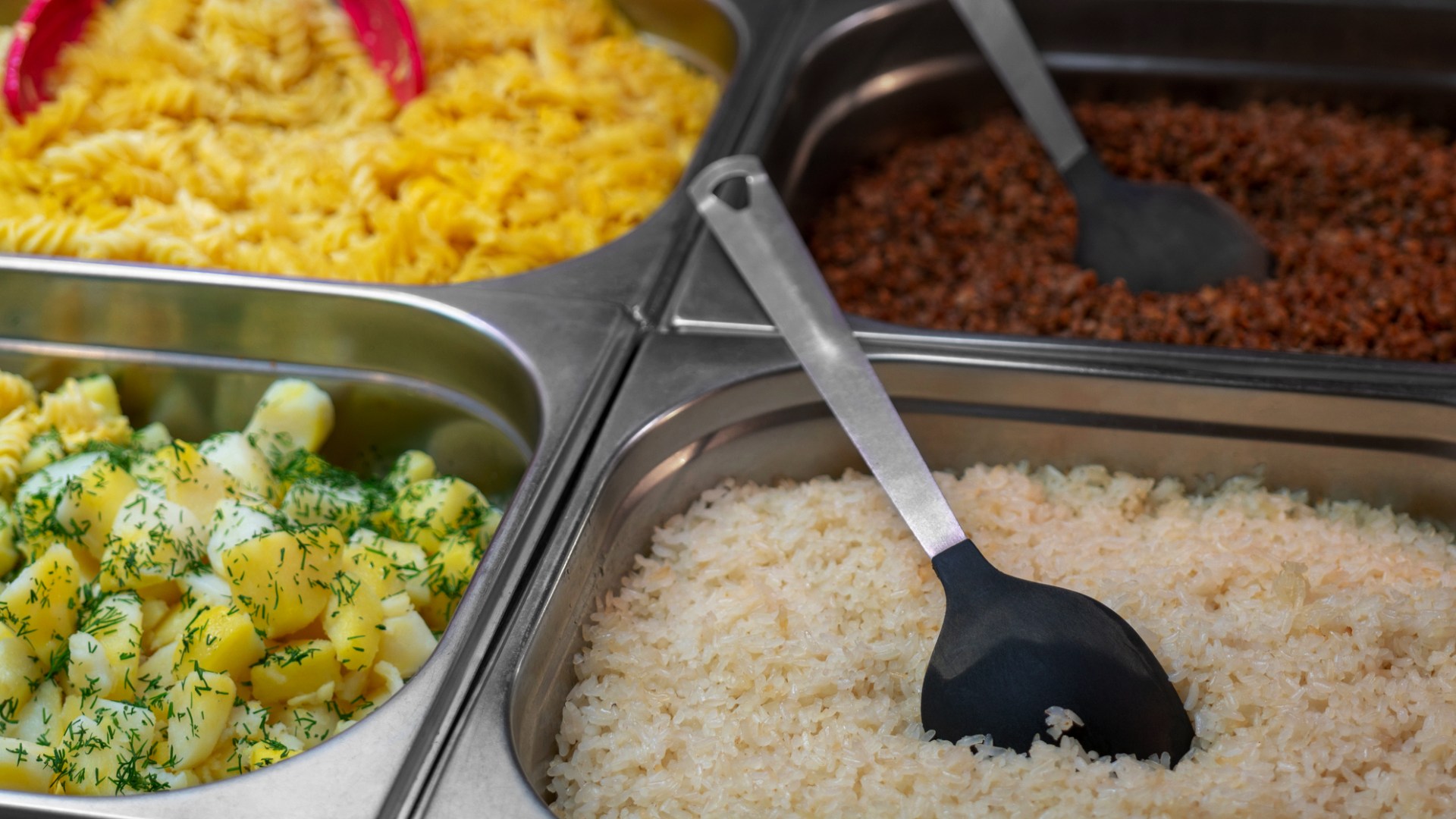 Ris, potatis, makaroner och röd sås i fyra metallbyttor, med slevar i.