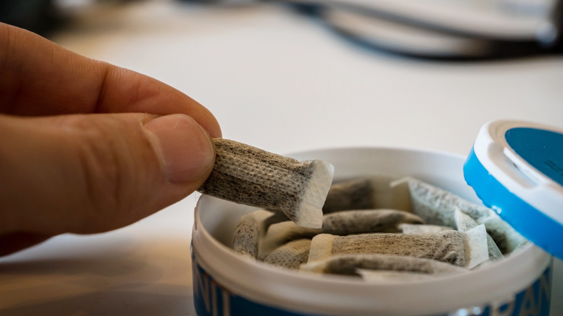 Hand greppar en snusprilla från en snusdosa med portionssnus.