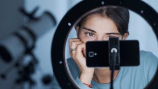 Ung kvinna tittar på mobiltelefon som sitter på ett stativ.