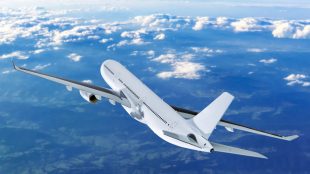 Vitt passagerarflygplan i luften, moln och mark lång bort.