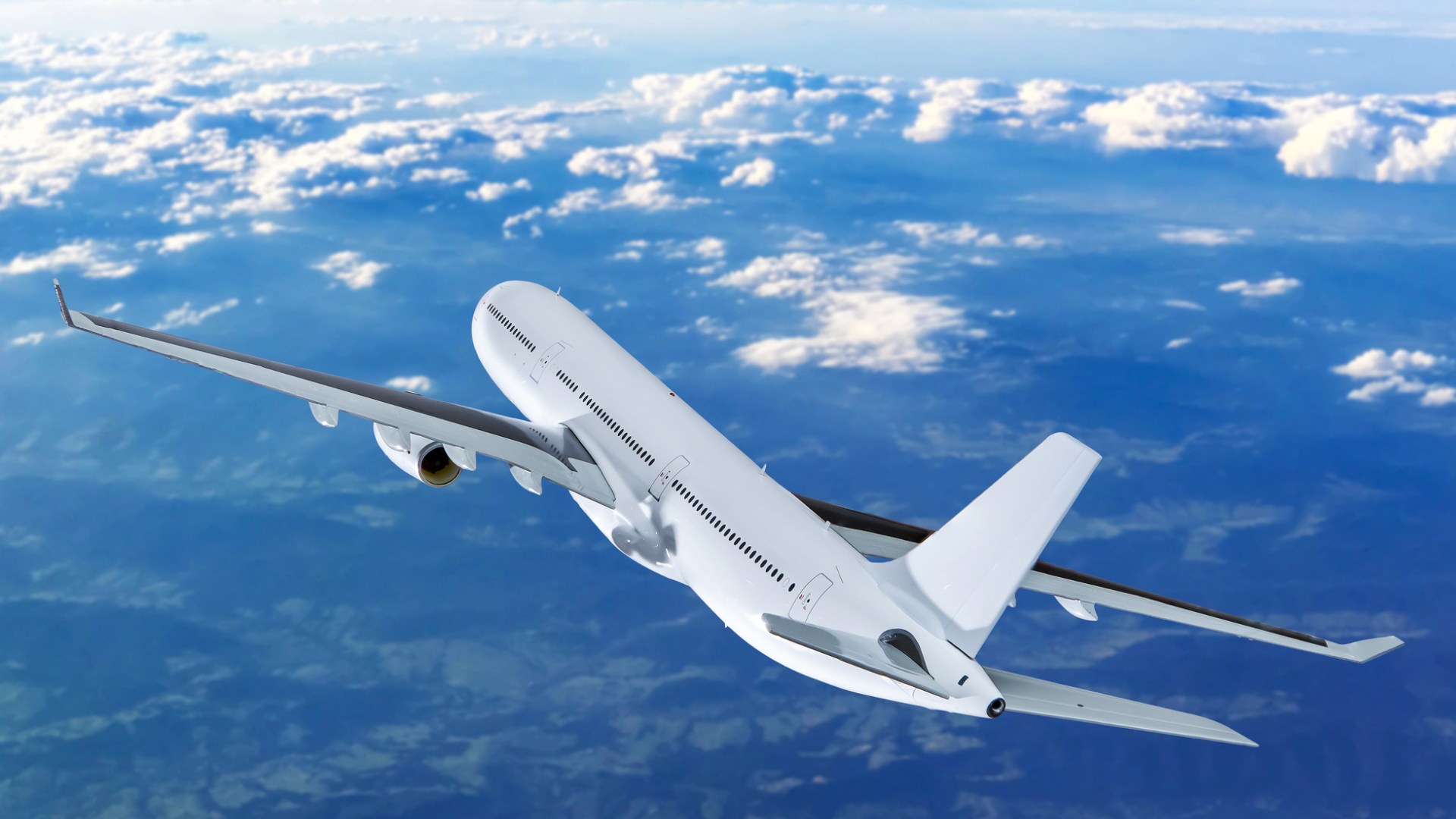 Vitt passagerarflygplan i luften, moln och mark lång bort.