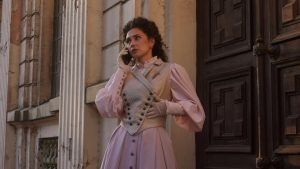 Kvinna i mycket gammaldags klänning och håruppsättning talar i mobiltelefon.