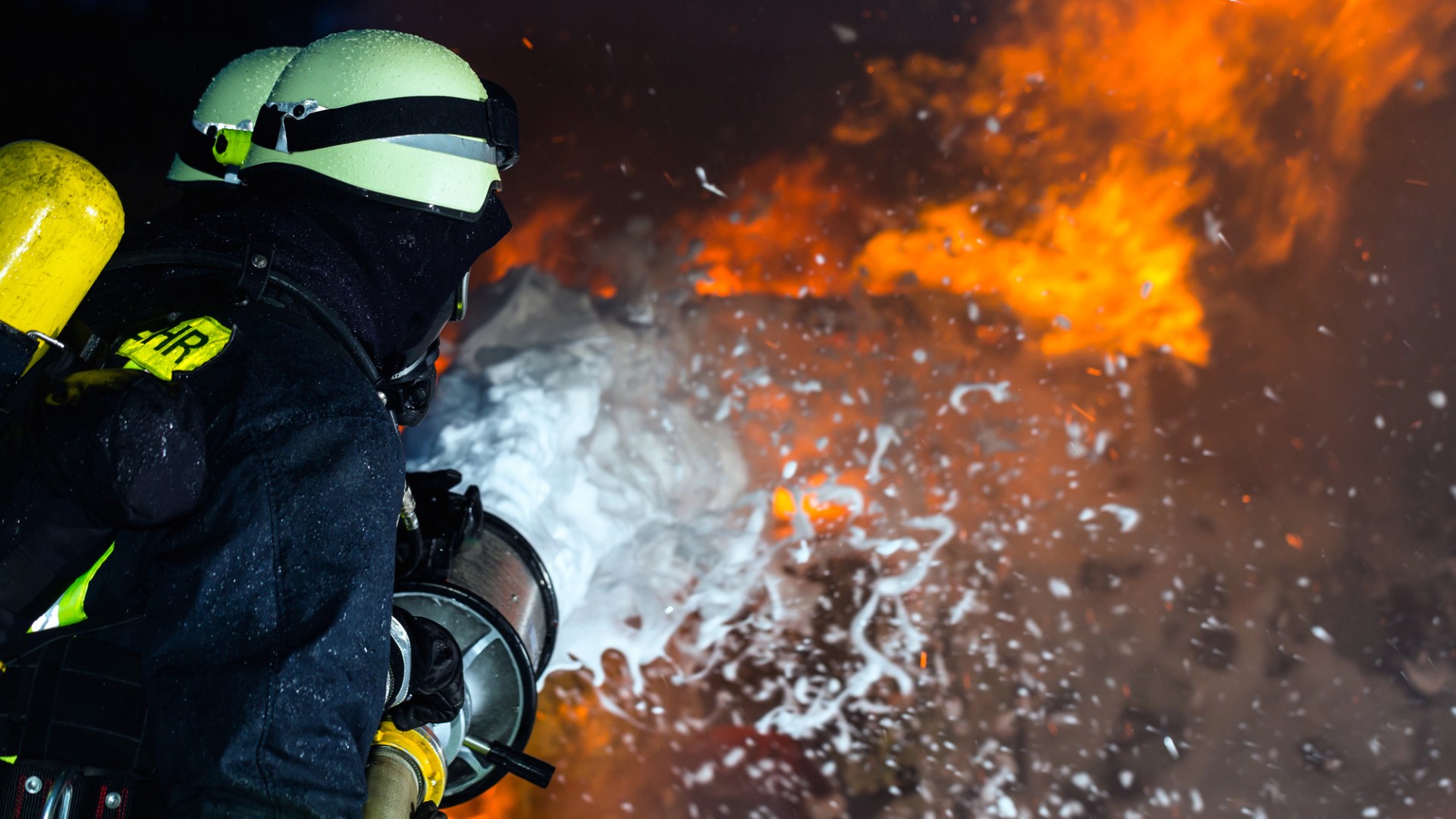 En brandman, bakifrån, som sprutar brandskum mot en eld.