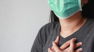 Kvinna med ansiktsmask håller händerna över hjärtat.