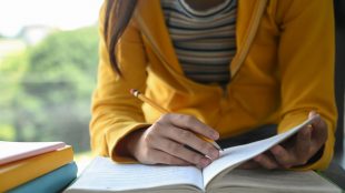 Flicka i gul tröja antecknar i ett skrivhäfte.