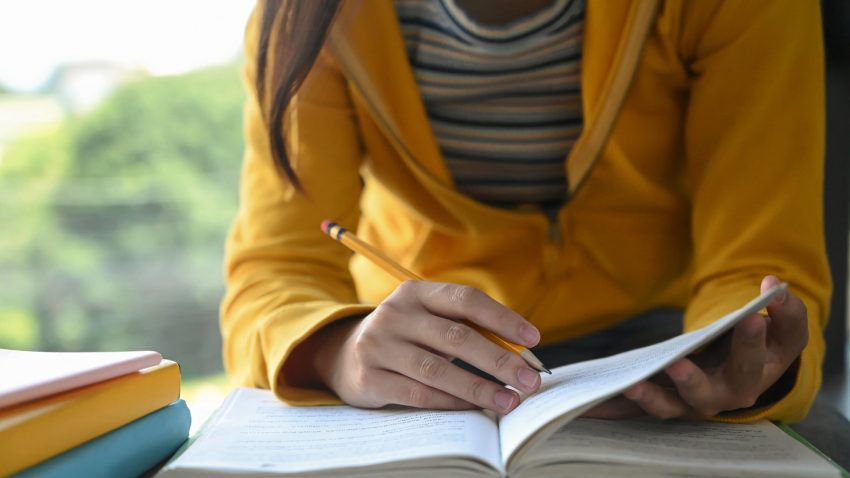 Flicka i gul tröja antecknar i ett skrivhäfte.