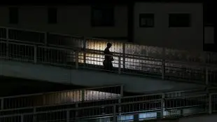 Ensam person går på bro i mörker, enstaka gatlyktor lyser upp.