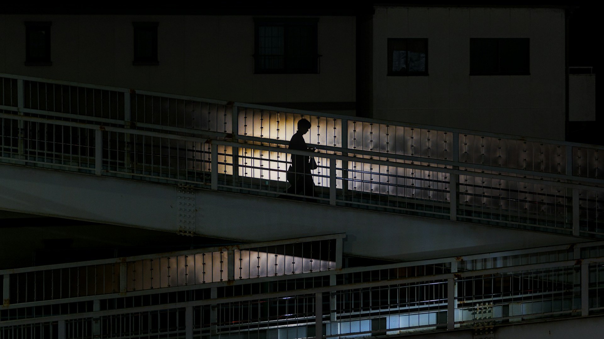 Ensam person går på bro i mörker, enstaka gatlyktor lyser upp.
