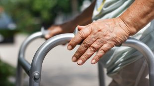 Äldre persons hand på rollator, utomhus.