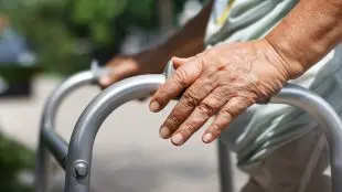 Äldre persons hand på rollator, utomhus.