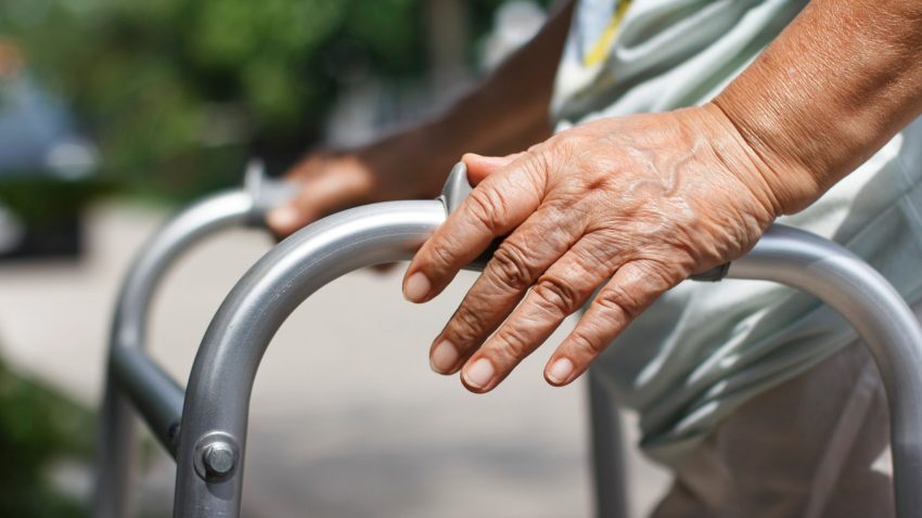 Äldre persons hand på rollator, utomhus.