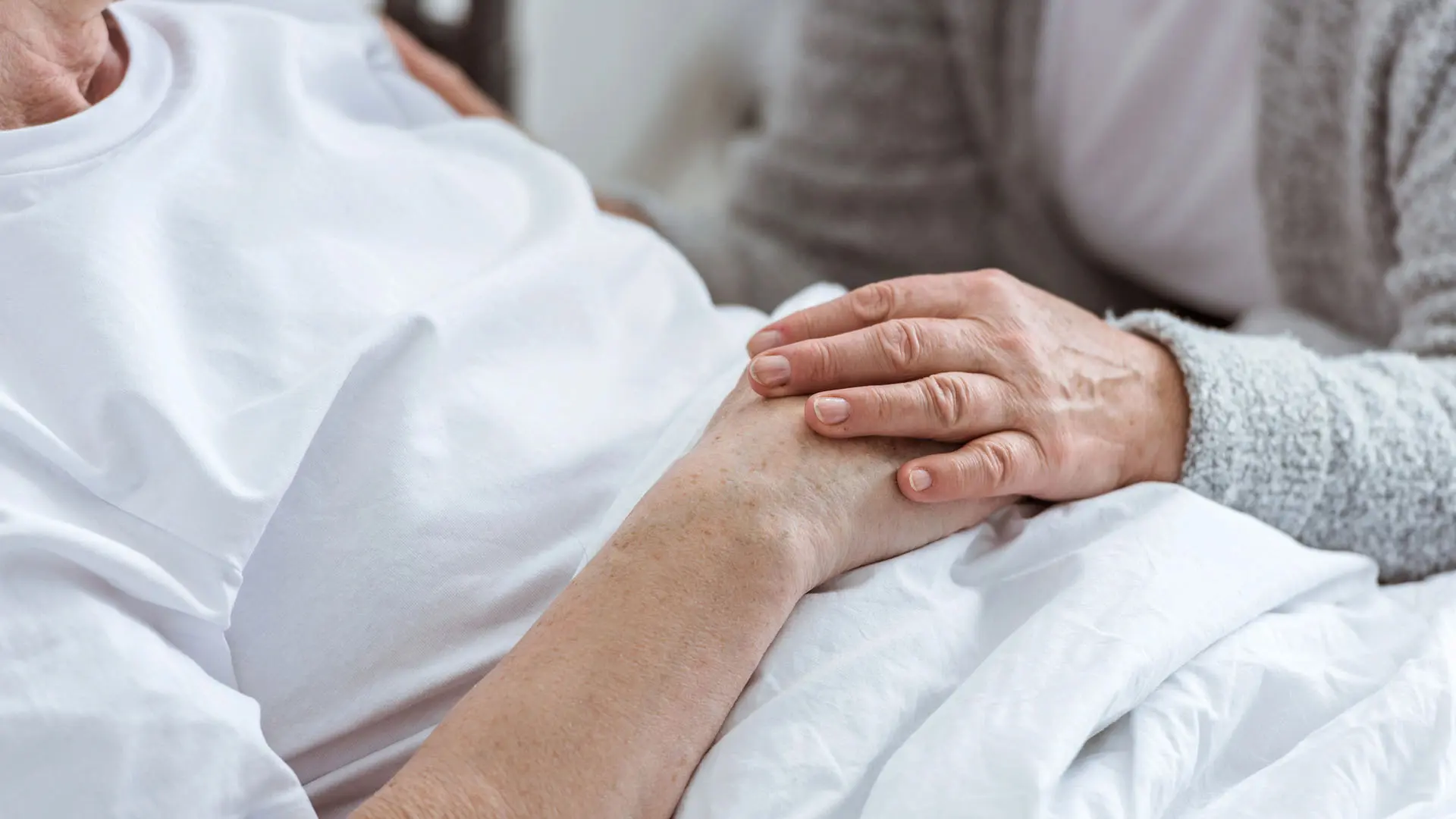Anhörig håller en sjuk persons hand.