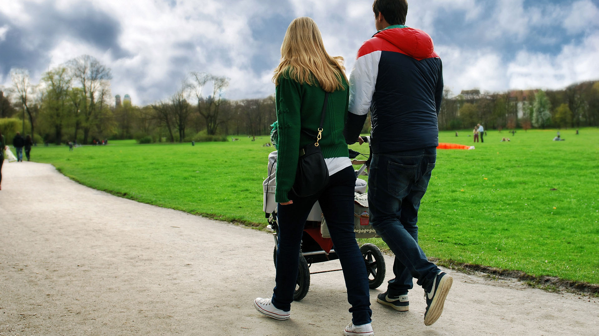 Föräldrar promenerar med barnvagn intill en park.