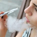 Ung kvinna i randig tröja röker en e-cigarett