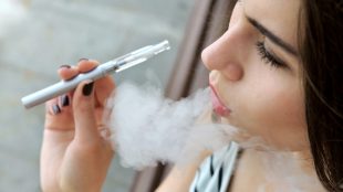 Ung kvinna i randig tröja röker en e-cigarett
