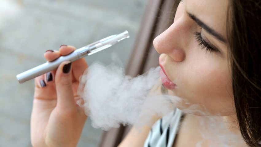 Ung kvinna i randig tröja röker en e-cigarett