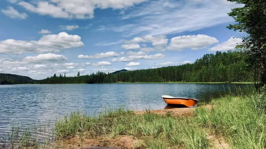 En orange båt ses vid stranden till en sjö.