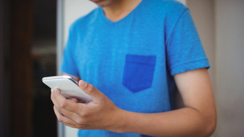 Tonårskille i blå t-shirt håller en mobil i händerna.