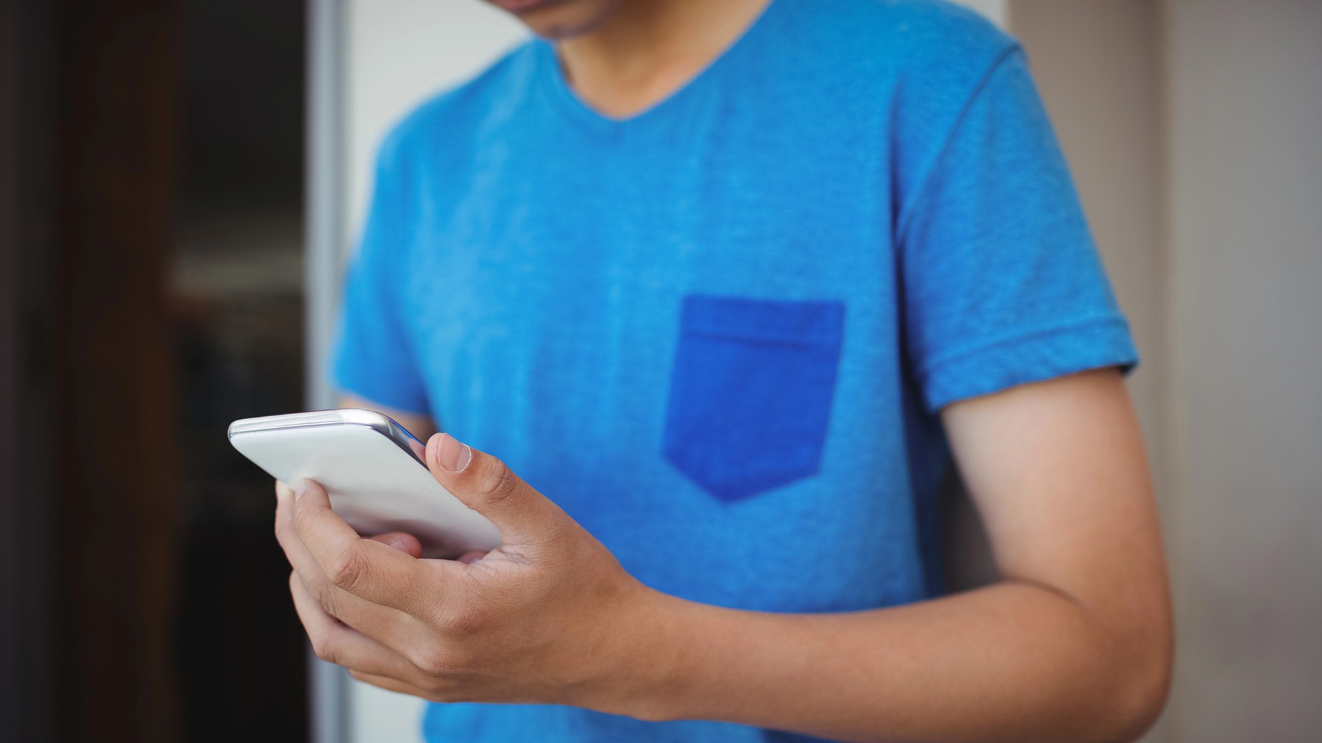 Tonårskille i blå t-shirt håller en mobil i händerna.