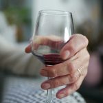 Äldre person sitter i en soffa med ett glas rött vin i handen.